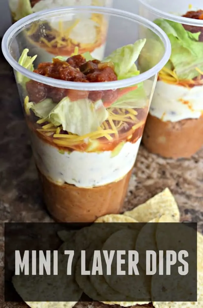 This photo is a photo of the seven layer dip in a cup. You can see all the different layers. There is a text overlay that says mini 7 layer dips.