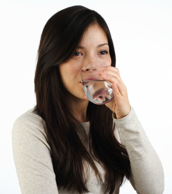 Female with long dark hair drinking water from a glass
