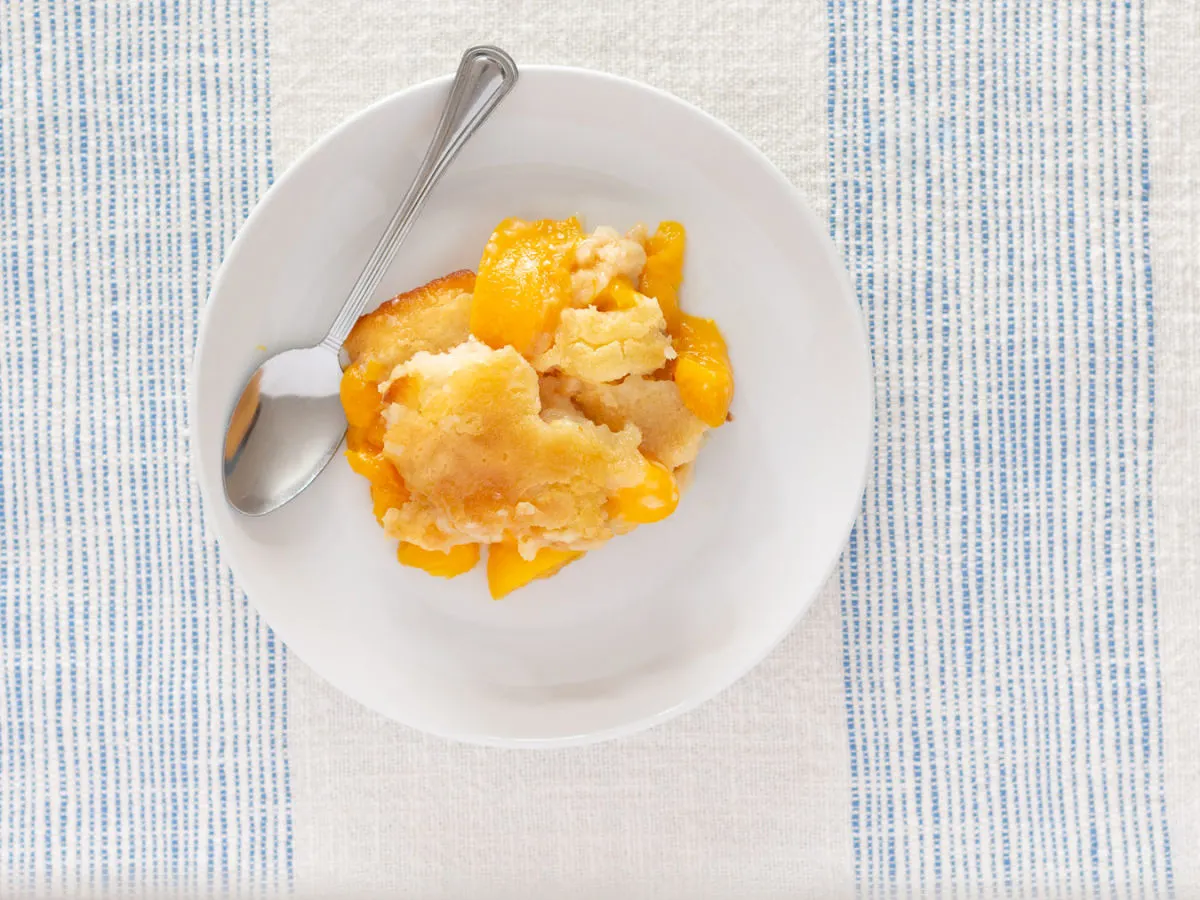 A white bowl served with golden brown peach cobbler. 