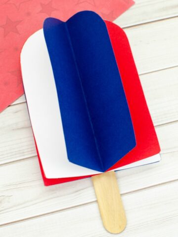 This photo features a popsicle stick popsicle craft. It uses red, white, and blue card stock paper to make a 3D popsicle.