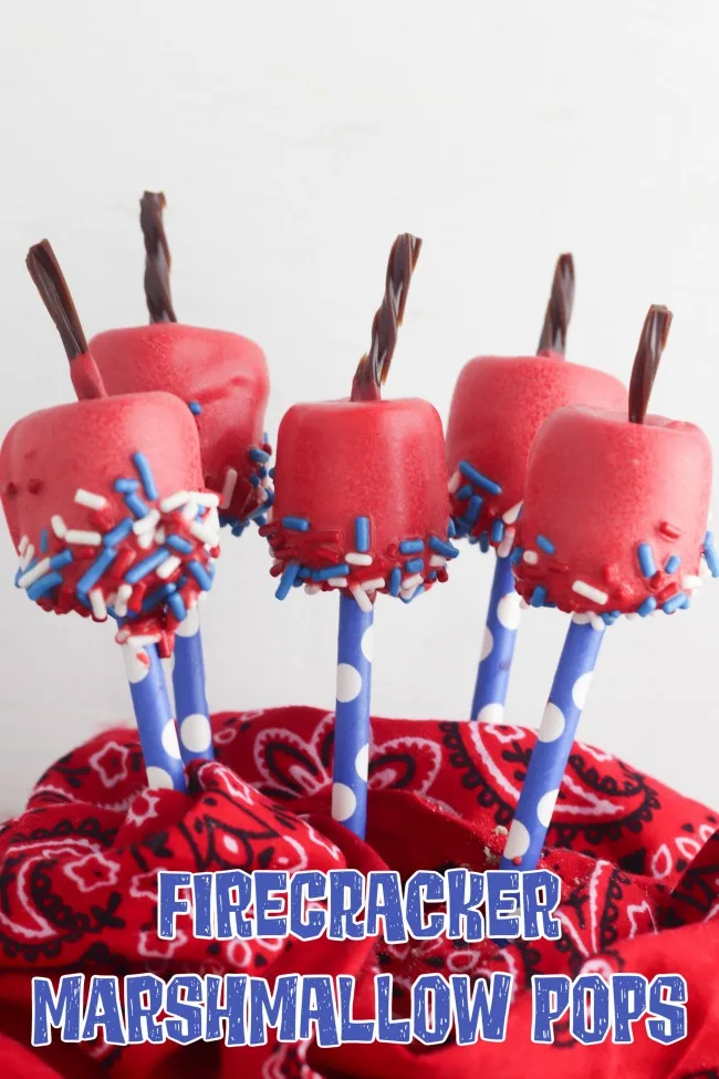 This photo features marshmallow treats that look like firecrackers. These firecracker marshmallow treats are covered in a red candy coating, dipped in red, white, and blue sprinkles, and topped with a piece of licorice for the "fuse"