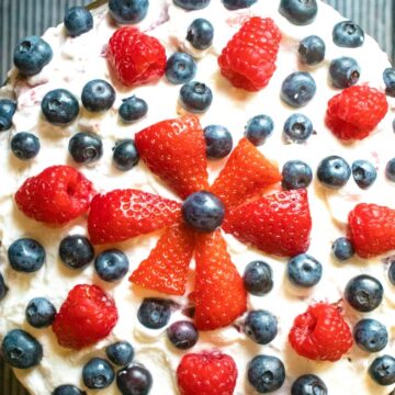 This photo features a above angle of a recipe called Raspberry Brandy Trifle. It is decorated with Strawberries, Raspberries, and Blueberries.