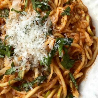 This photo features a white plate full of arrabbiata sauce with zucchini noodles topped with freshly grated parmesan.