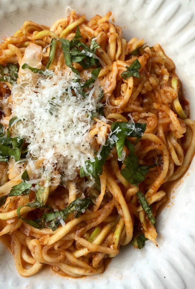 This photo features a white plate full of arrabbiata sauce with zucchini noodles topped with freshly grated parmesan.