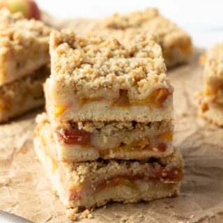 This photo features a stack of peach crumble bars sitting on a crumbled brown paper bag.