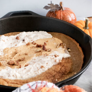 This photo features a pumpkin spice dutch baby in a cast iron skillet. It is topped with pumpkin mousee and maple whipped cream.