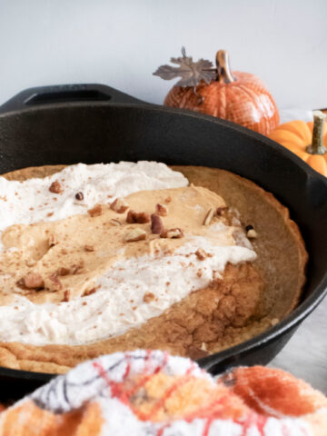 This photo features a pumpkin spice dutch baby in a cast iron skillet. It is topped with pumpkin mousee and maple whipped cream.