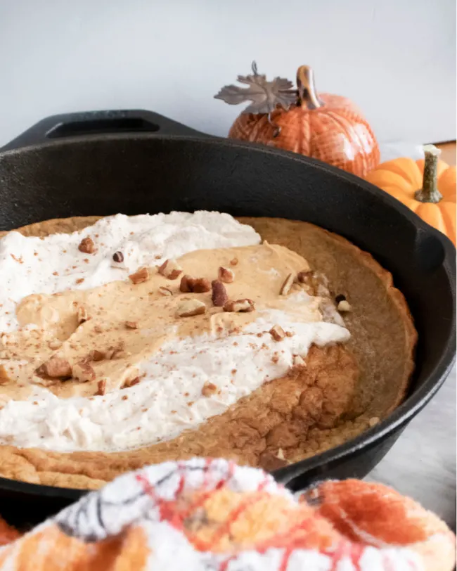 This photo features a pumpkin spice dutch baby in a cast iron skillet. It is topped with pumpkin mousee and maple whipped cream. 
