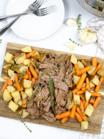 This photo features a cutting board topped with pot roast and all the veggie sides.