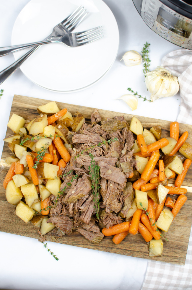 This photo features a cutting board topped with pot roast and all the veggie sides.