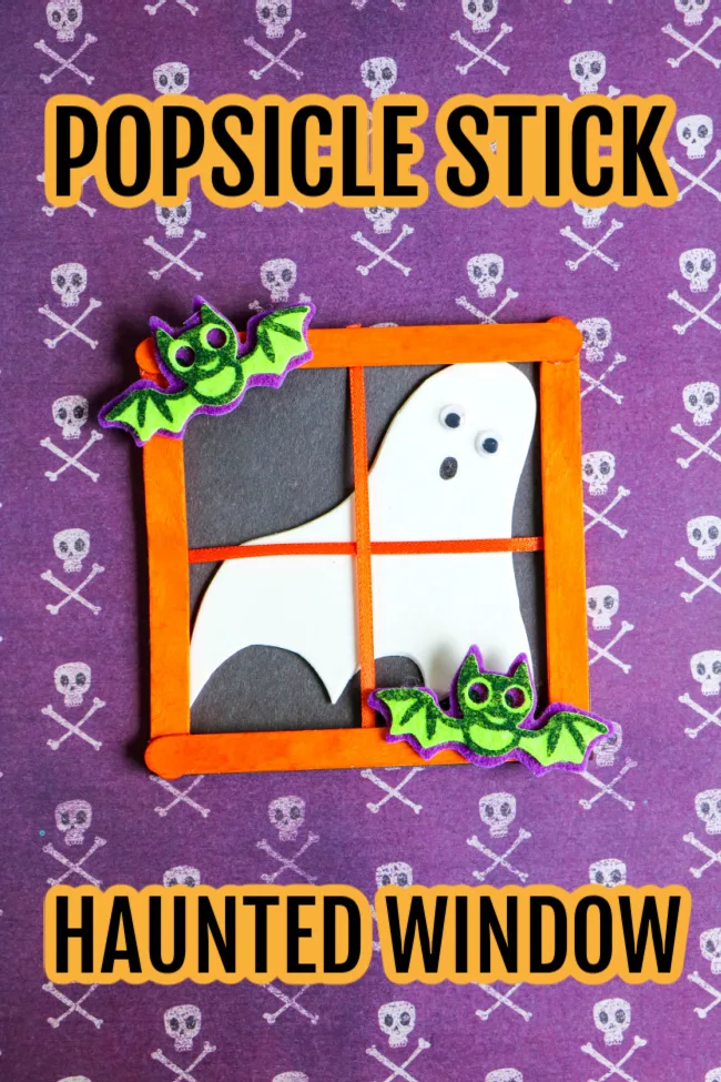 This image features a Halloween craft for kids at looks like a popsicle stick haunted window. It is laying on top of Halloween skull craft paper.