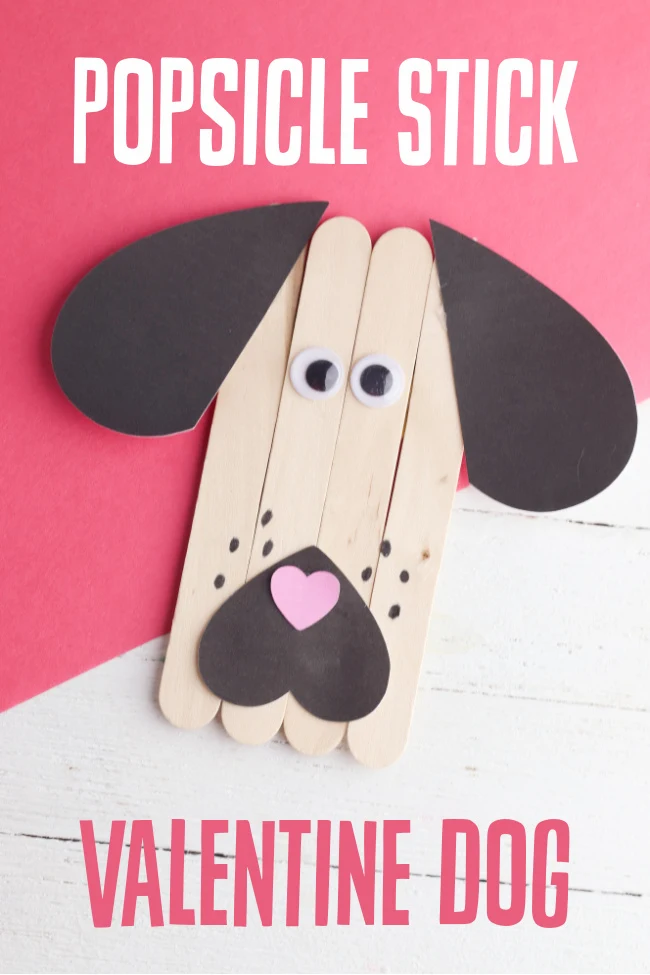 This photo features a created popsicle stick dog Valentine craft on top of a white and red background.