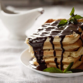 A white plate topped with a stack of waffles that are drizzled with chocolate gravy. The gravy boat in the background.