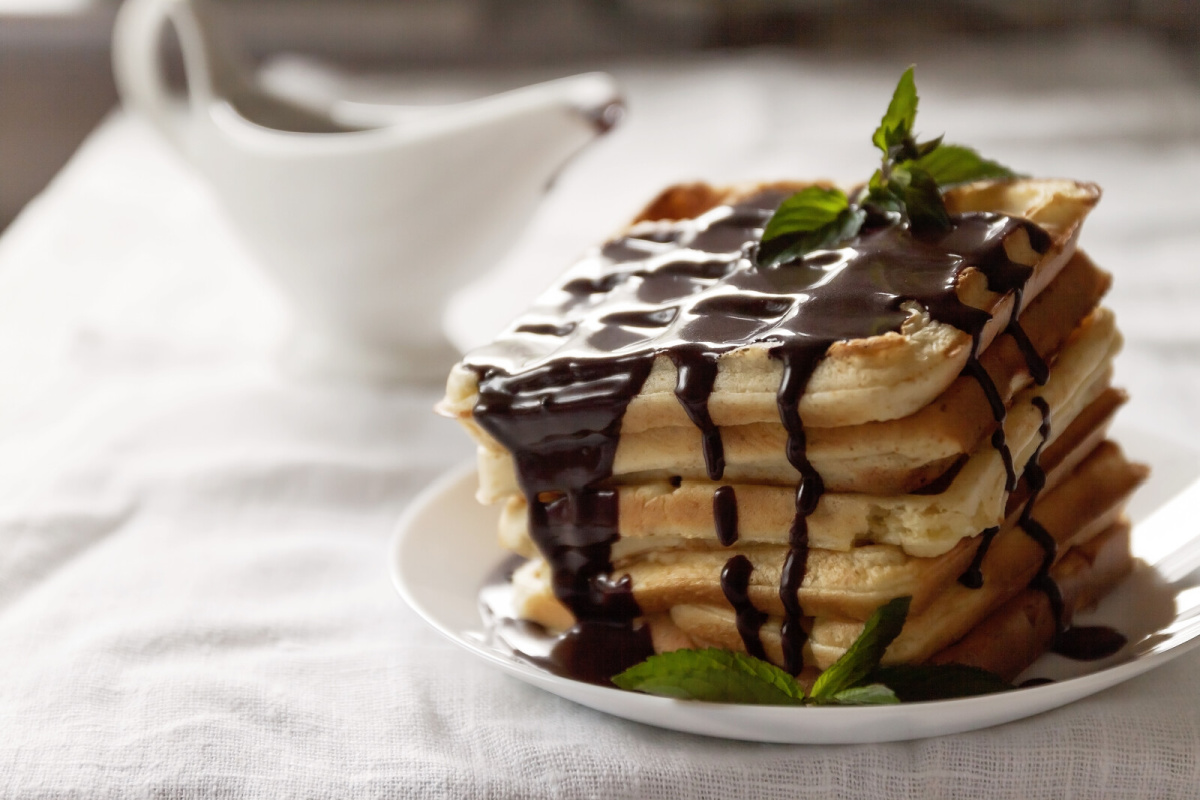 A white plate topped with a stack of waffles that are drizzled with chocolate gravy. The gravy boat in the background.