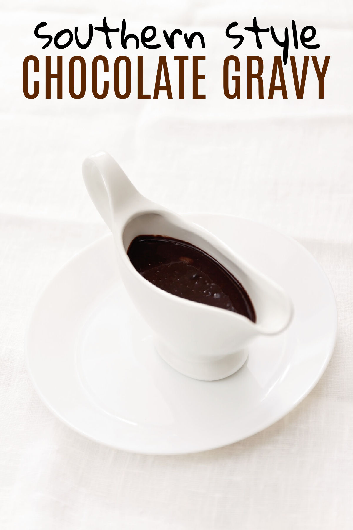 A white gravy boat filled with chocolate gravy sitting on a white plate with a white background