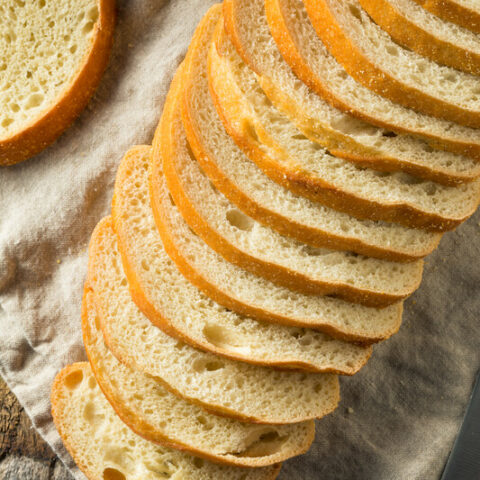 This photo features an arrangement of sliced sourdough bread on top of a wooden board and brown tea towel.