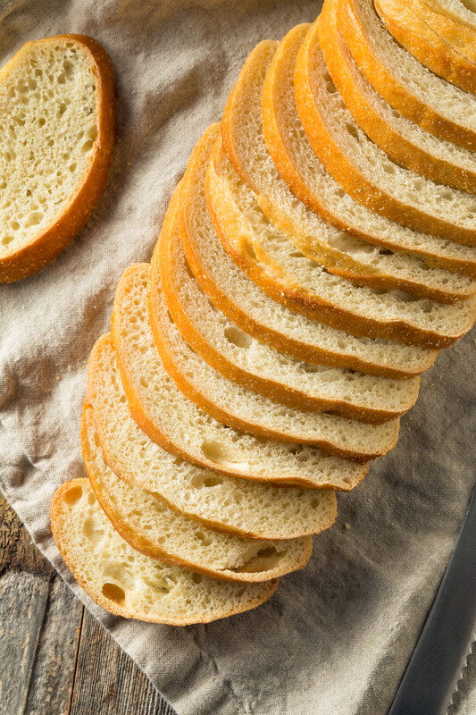 This photo features an arrangement of sliced sourdough bread on top of a wooden board and brown tea towel.