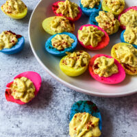 A plate full of dyed deviled eggs on a concrete background