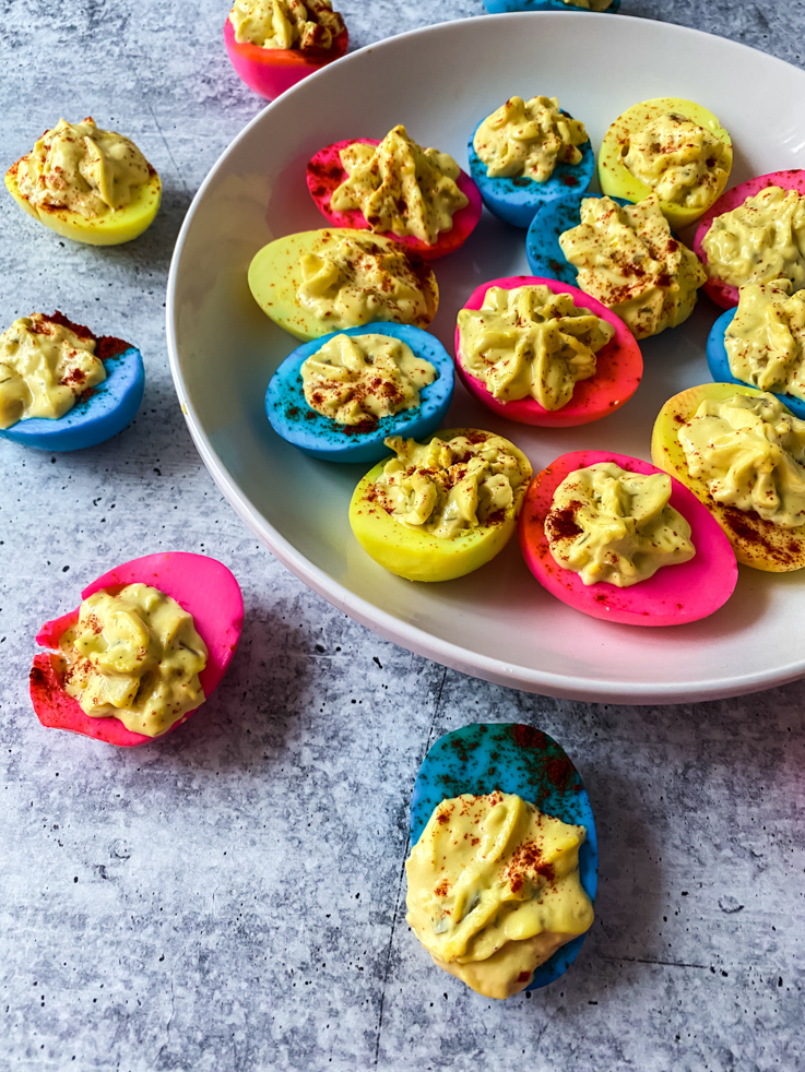 A plate full of dyed deviled eggs on a concrete background