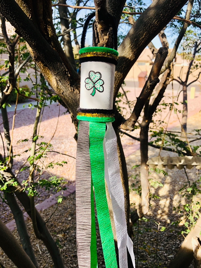 This photo features a completed St. Patrick's Day Windsock toilet paper roll craft hanging in a tree ready to catch the breeze from the wind.