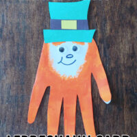A crafted handprint leprechaun card on a wood background