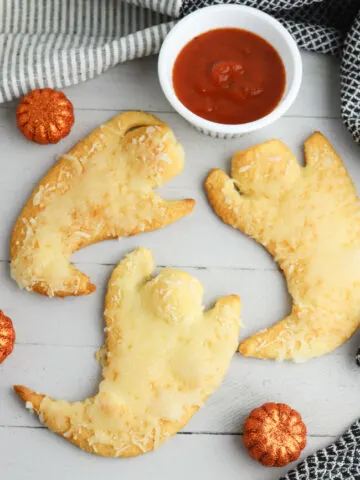 Cheesy Ghost Crescent Rolls on a white background with maranara dipping sauce