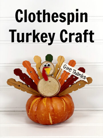 Clothespin Turkey craft sitting on top of a faux orange pumpkin with a white wood slate background.