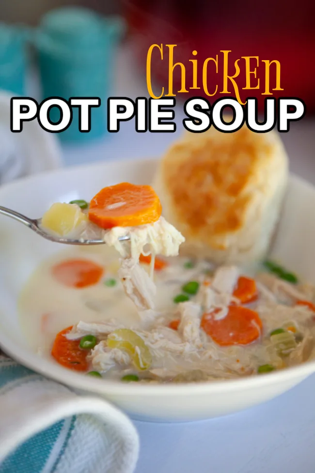 A white bowl with Chicken Pot Pie Soup inside with a biscuit on the side of the bowl.