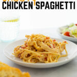 A white plate of cheesy chicken spaghetti on a marble table. In the foreground is a plate of side salad and Texas toast