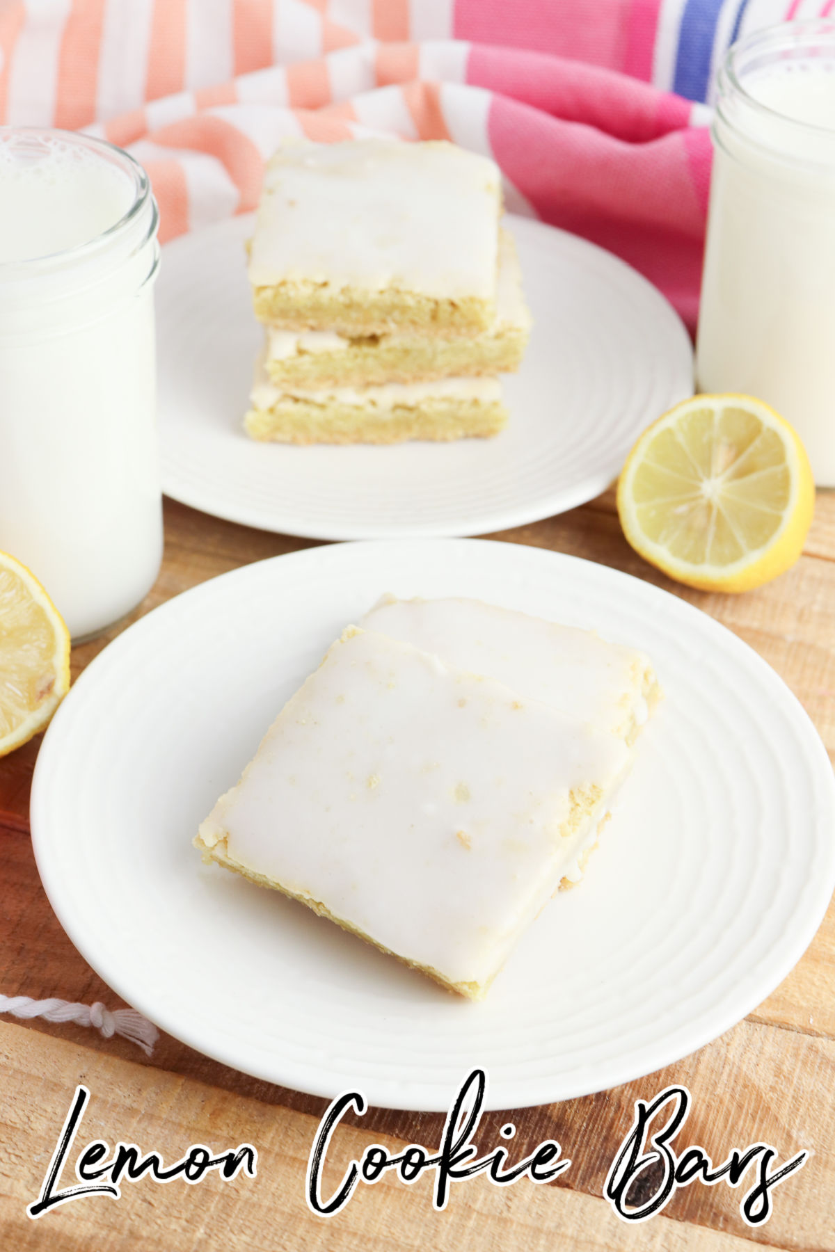a white plate of lemon cookie bars with stacked cookie bars in the back and a sliced lemon on the side
