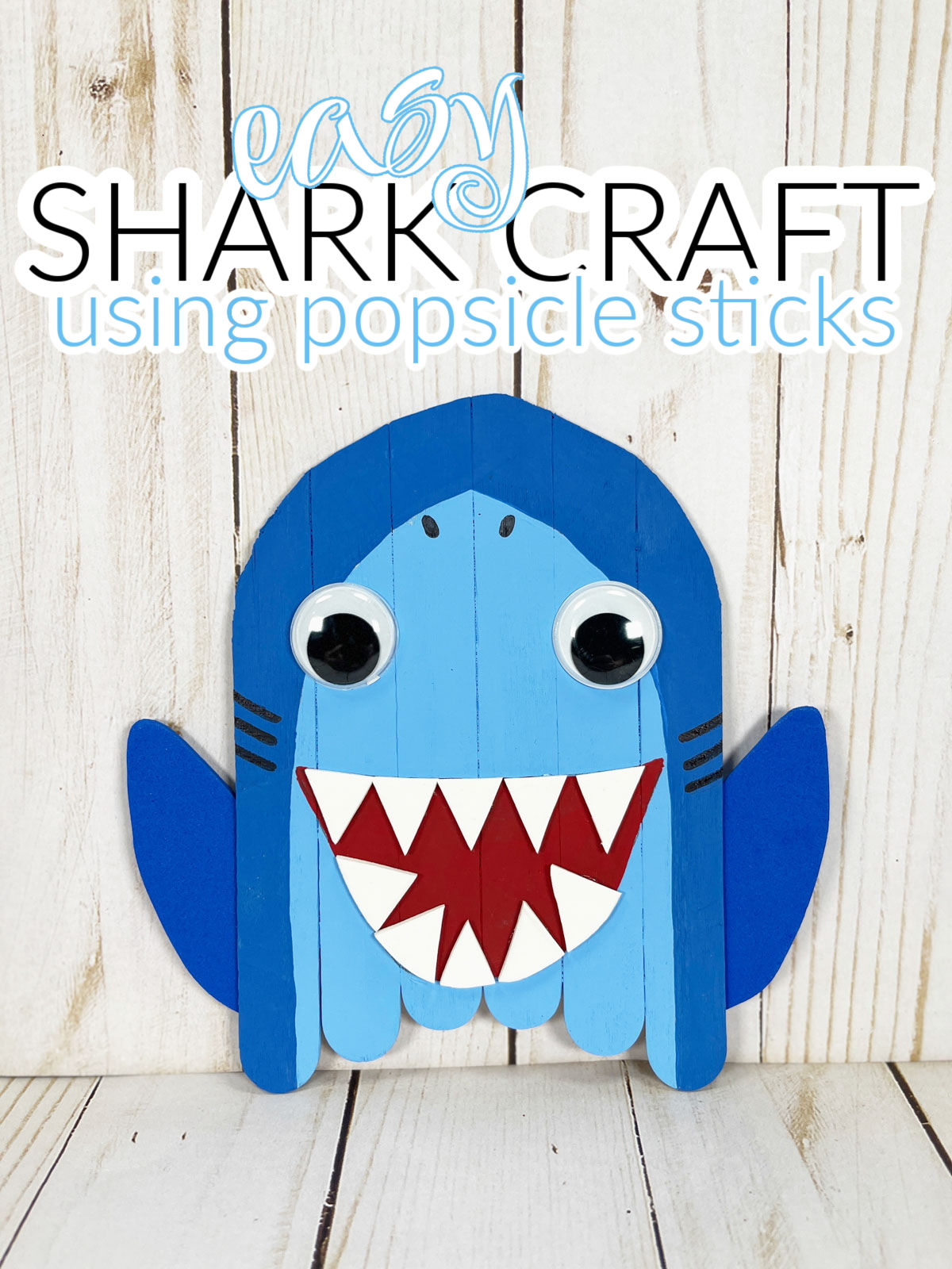 Easy Shark Craft made using popsicle sticks on a white wooden background.