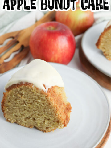 A slice of apple bundt cake on a white plate with a whole apple in the background.