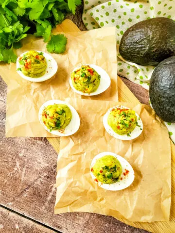 Avocado Deviled Eggs on brown paper and avocados sitting to the side.