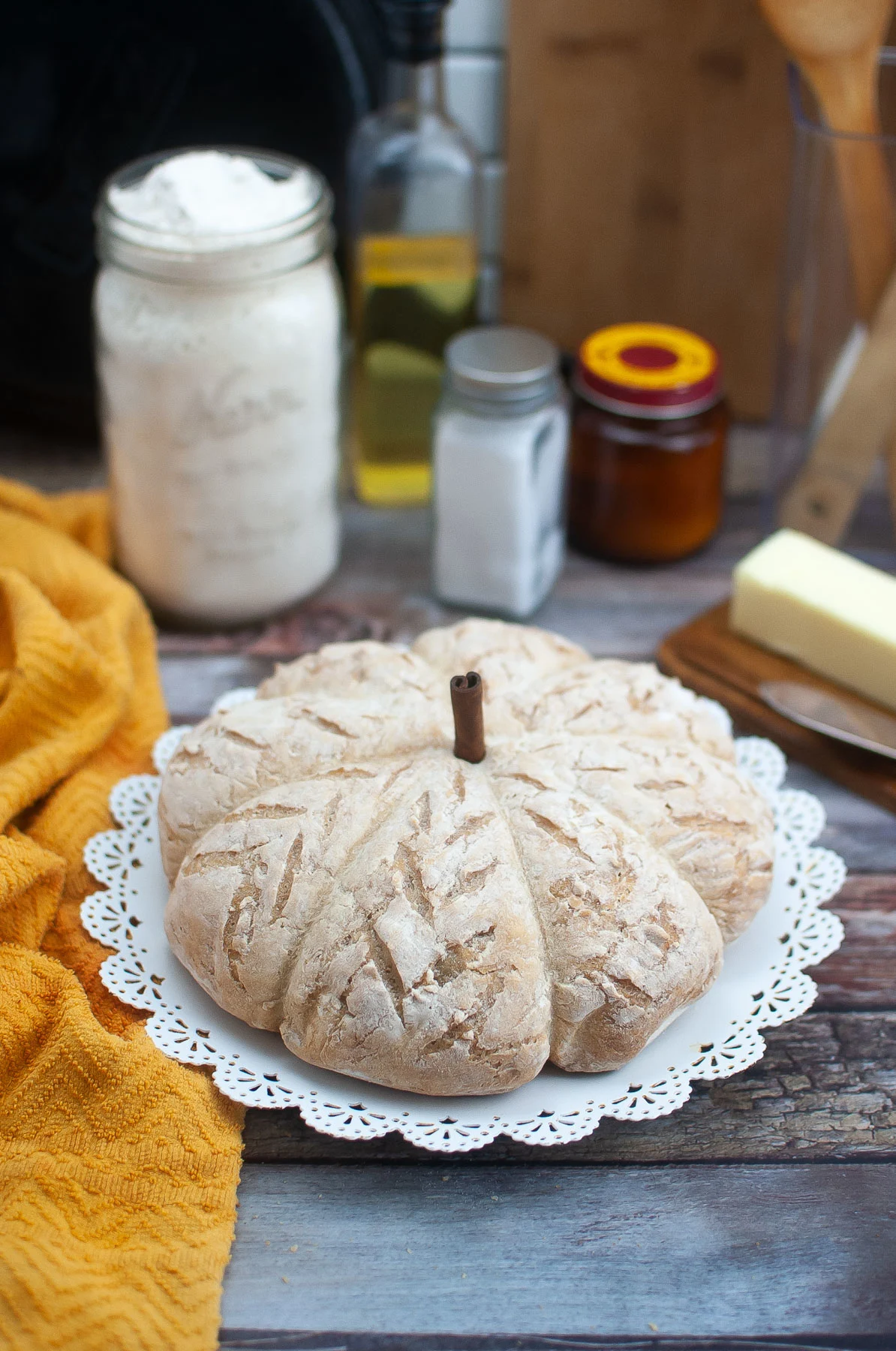 A pumpkin shaped bread on a white doily plate with a cinnamon stick placed in the top.